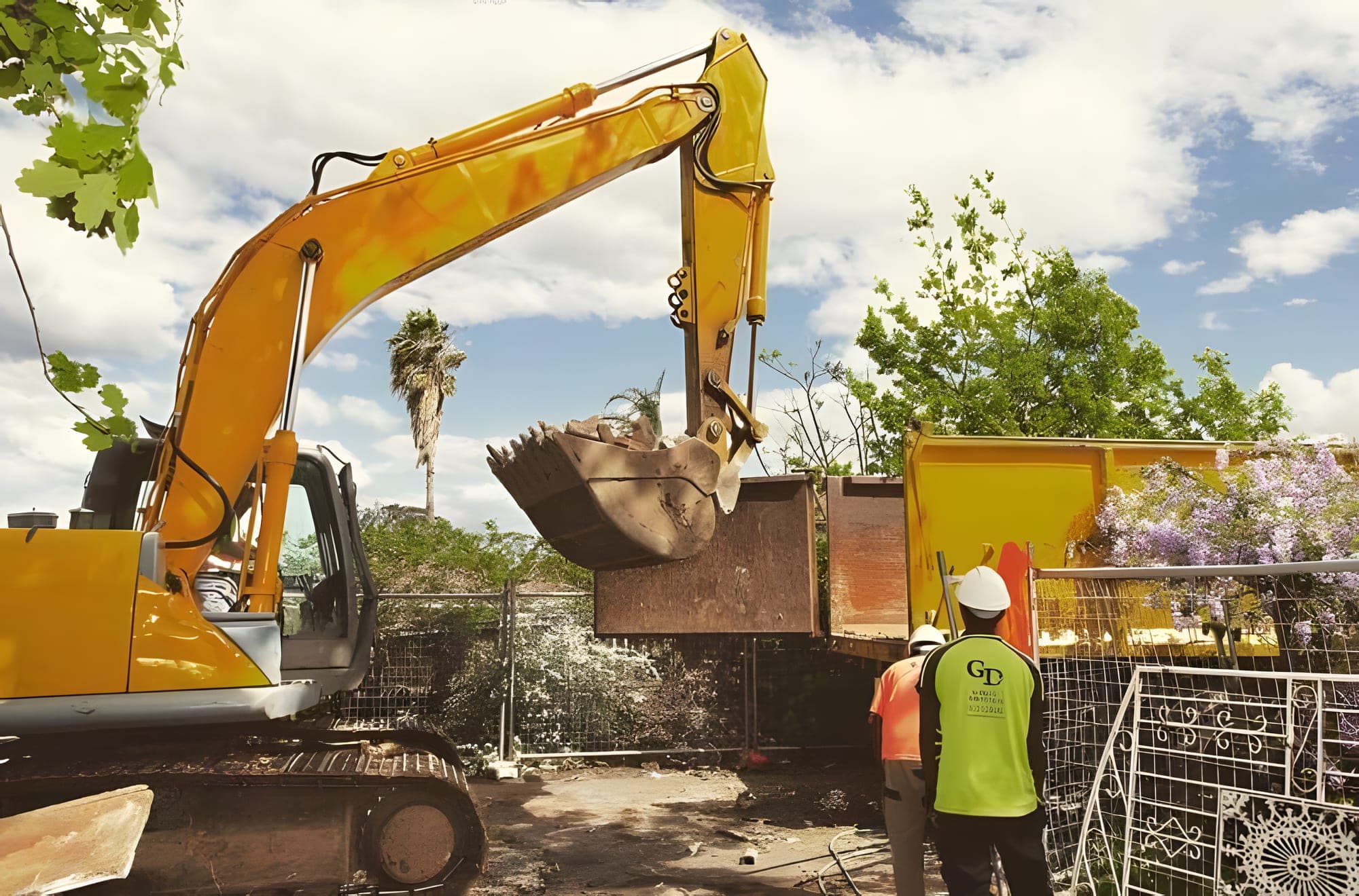 Gabrael excavator loading demolition material into a tipper truck while two crew members in hard hats watch on