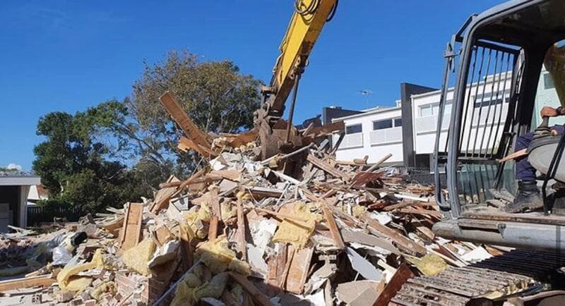 Excavator working through timber and masonry from a house structure