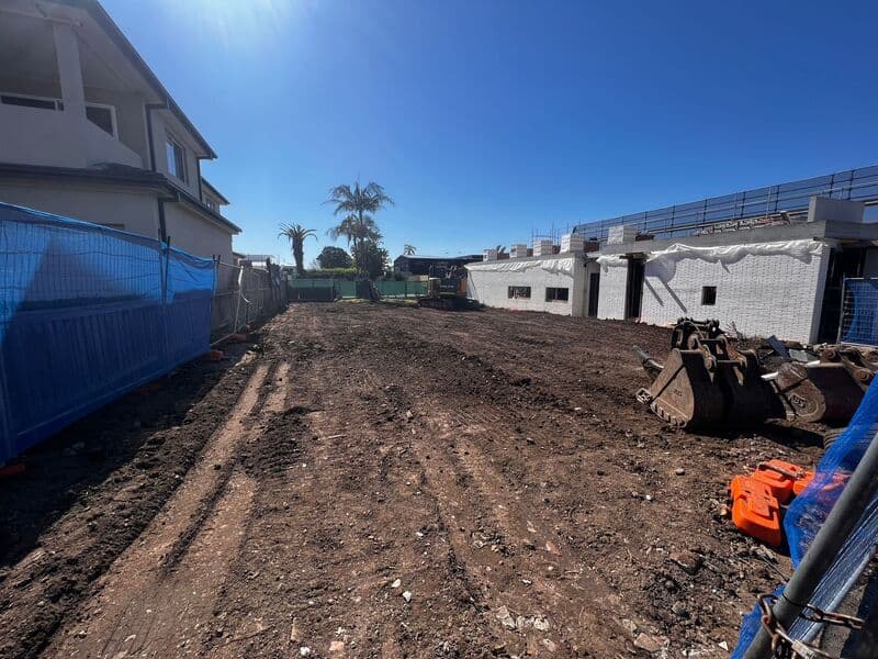 Cleared ground with machinery along the right-hand boundary and buildings beyond