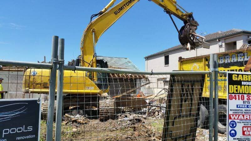 Excavator above a Gabrael truck behind temporary site fencing