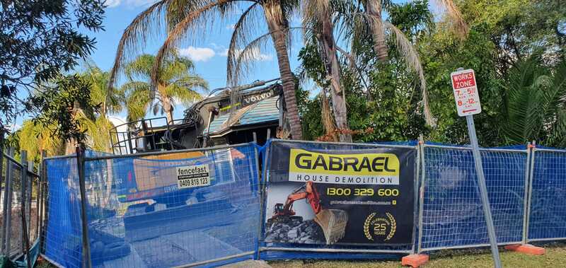 Excavator at a residential property behind blue mesh fencing and Gabrael signage