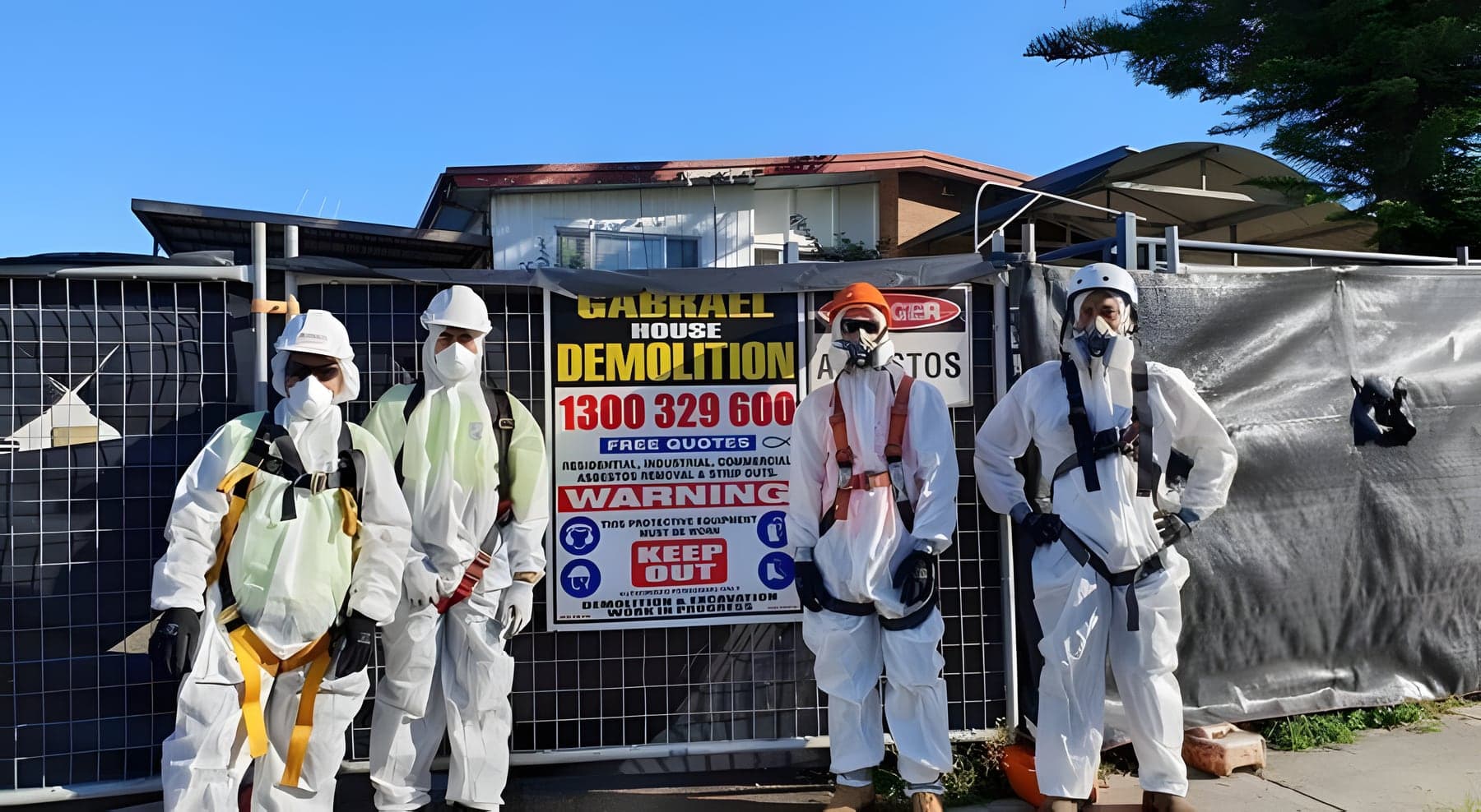 Four Gabrael crew members in asbestos protective suits and respirators beside Gabrael Demolition signage on the site fence